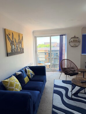 Ein Wohnzimmer mit einem blauen Sofa, einem gemusterten Teppich, einem Sessel und einem Gemälde von Eseln.
