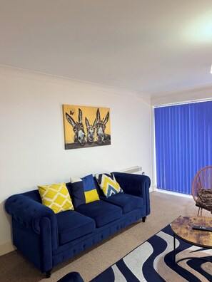 A living room with a blue sofa, patterned cushions, a rug, and a painting of donkeys. - Stylish City-Centre Apartment Your Perfect Birmingham Base (Birmingham)