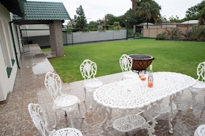 An outdoor patio with a round table, white chairs, and a barbecue grill.