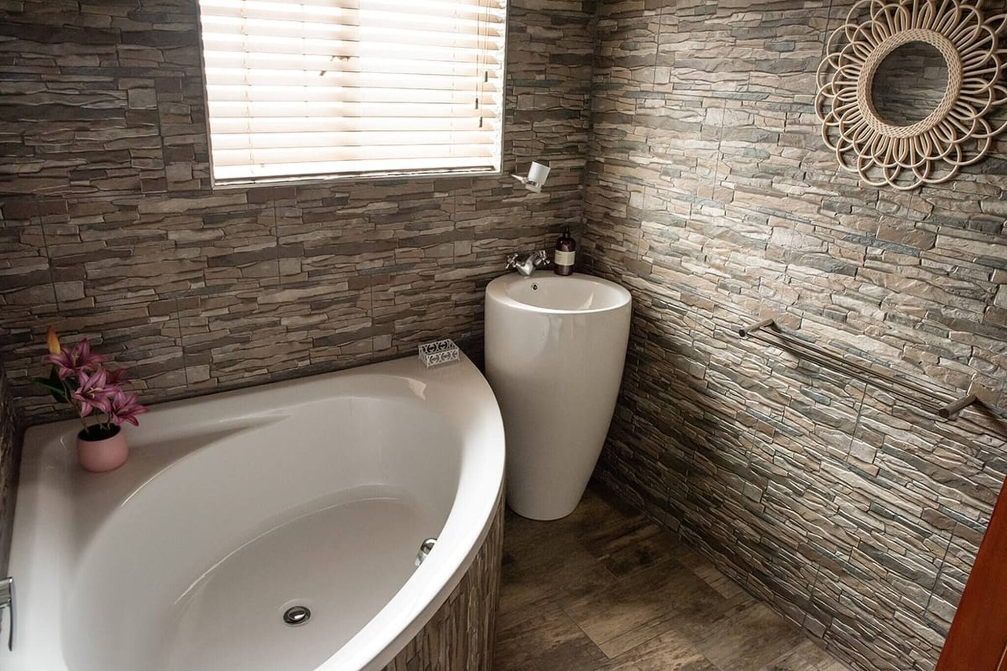 A bathroom with a stone wall, a large bathtub, a sink, and a decorative mirror.
