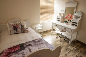 Un dormitorio con cama, cómoda, tocador con espejo y ventana con persianas.