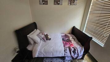 A bed with a floral bedspread, a white pillow, and a dark headboard. There are three wall-mounted pictures above the bed.