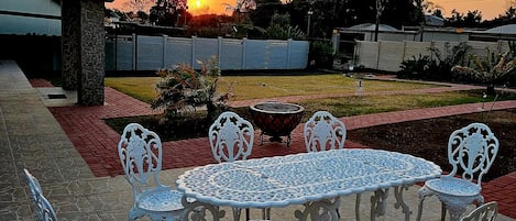Un patio exterior con una mesa redonda y sillas, una parrilla y una puesta de sol al fondo.