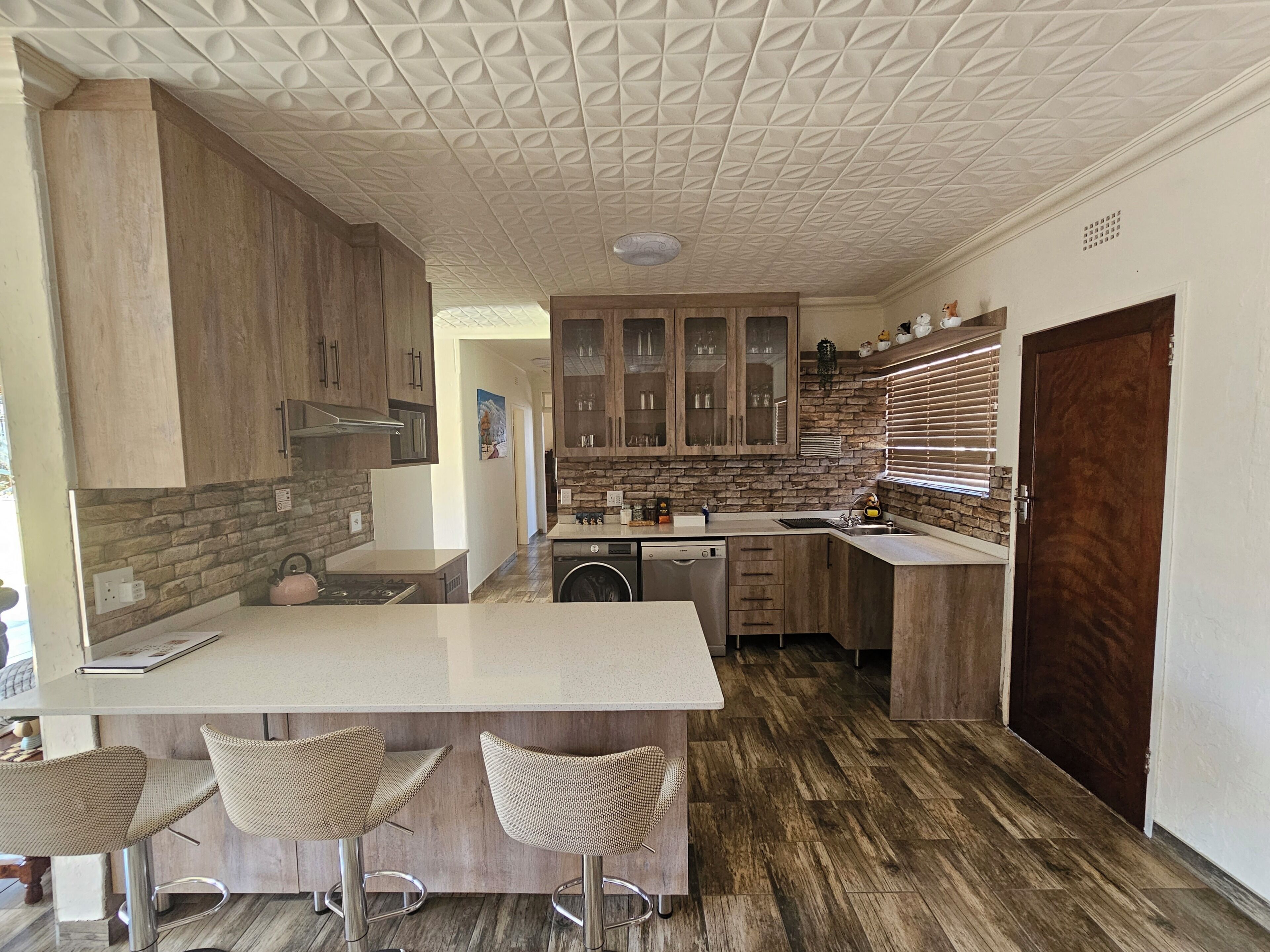 A modern kitchen with a central island, bar stools, wooden cabinets, and a stone backsplash.