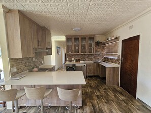 A modern kitchen with a central island, bar stools, wooden cabinets, and a stone backsplash.