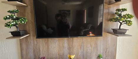 Un meuble de rangement en bois pour appareils multimédias, avec un téléviseur à écran plat, des plantes en pot et une petite figurine de chien.