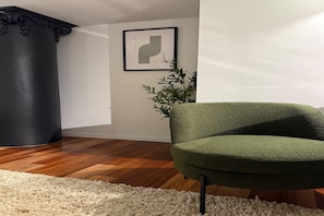 A room with a green armchair, a white rug, a wooden floor, a dark-colored column, and a framed picture on the wall. - Heritage Loft | Degraves Lane Melbourne CBD (Melbourne)