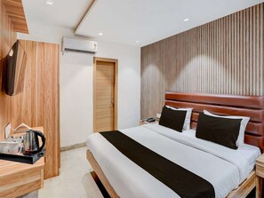 Ein modernes Hotelzimmer mit einem Holzkopfteil, einem flachbildfernseher an der Wand, einem Nachttisch mit Wasserkocher und Tassen sowie einer Holztür.
