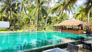 A pool area with lounge chairs and a bar, surrounded by palm trees.