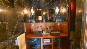 Une salle de bain avec des murs en marbre, deux lavabos, un porte-serviettes et une étagère contenant des articles de toilette.