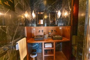 Ein Badezimmer mit Marmorwänden, zwei Waschbecken, einem Handtuchhalter und einem Ablagebereich für Pflegeprodukte.