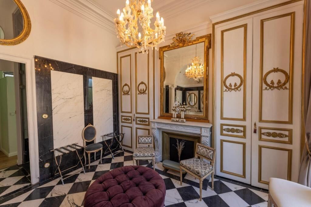 A room with a checkered floor, a fireplace, a mirror, and a chandelier.