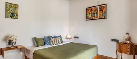 A bedroom with a bed, bedside table, lamp, and artwork on the walls.