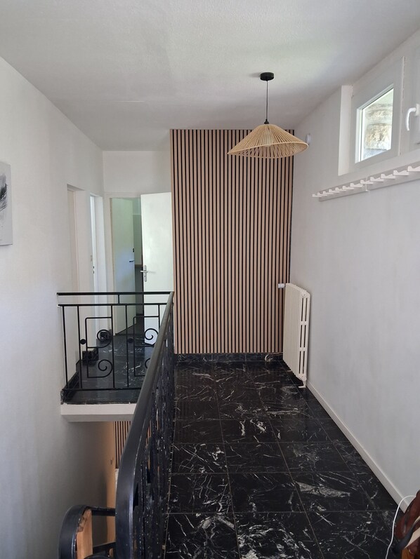 A hallway with a black marble floor, a striped wall, a white radiator, and a hanging light fixture.