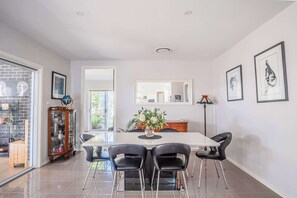 Un comedor con una mesa blanca, sillas negras y un jarrón con flores.