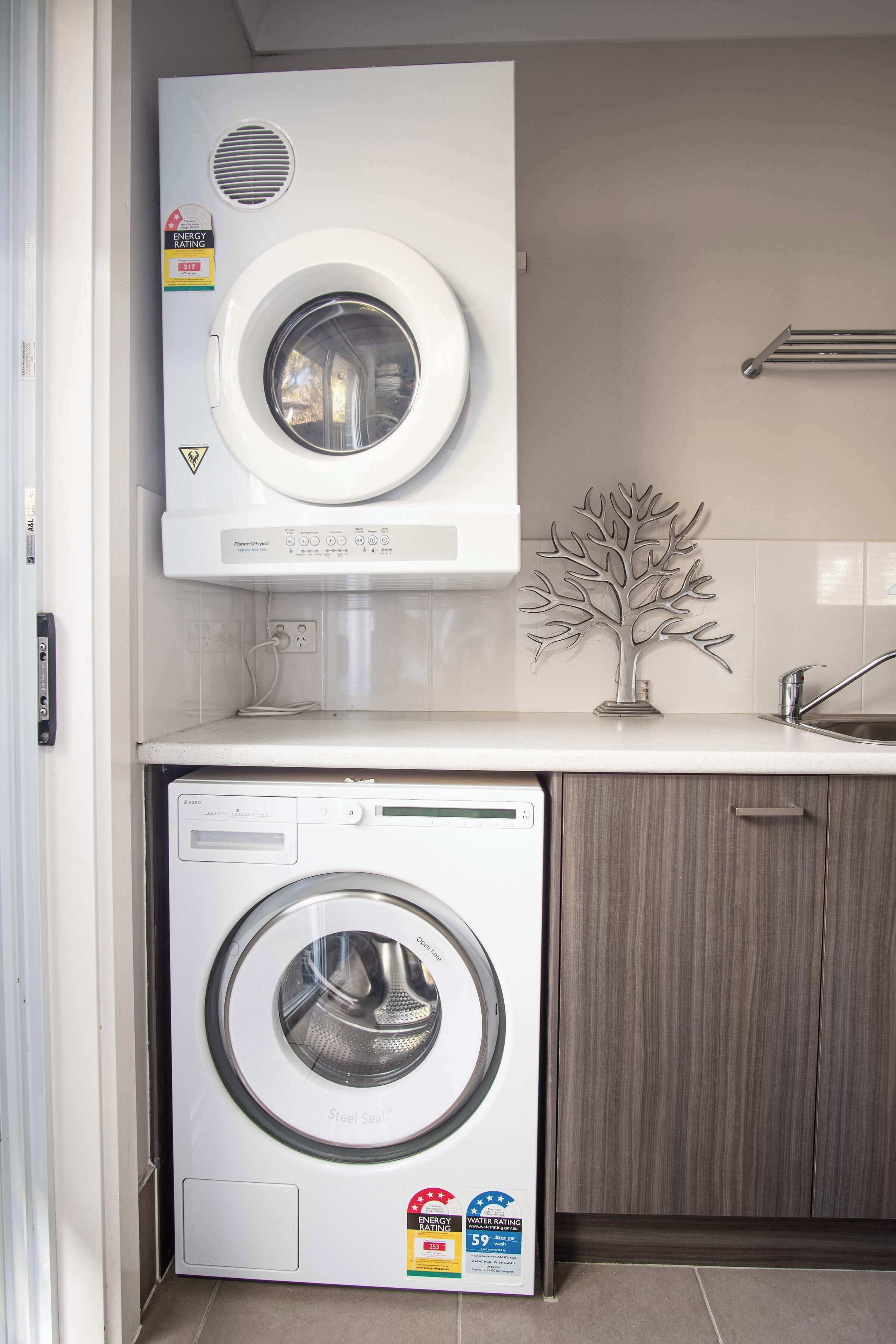 A compact laundry area with a front-loading washing machine and a top-loading dryer, both with energy and water rating labels.