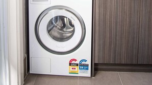 Ein kleiner Waschbereich mit einer Waschmaschine mit Frontlader und einem Trockner mit Oberlader, beide mit Kennzeichnungen für Energieeffizienz und Wasserverbrauch.