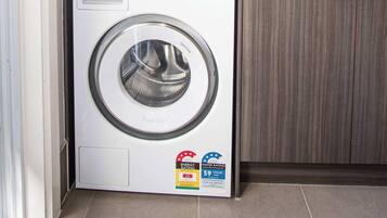 A compact laundry area with a front-loading washing machine and a top-loading dryer, both with energy and water rating labels.