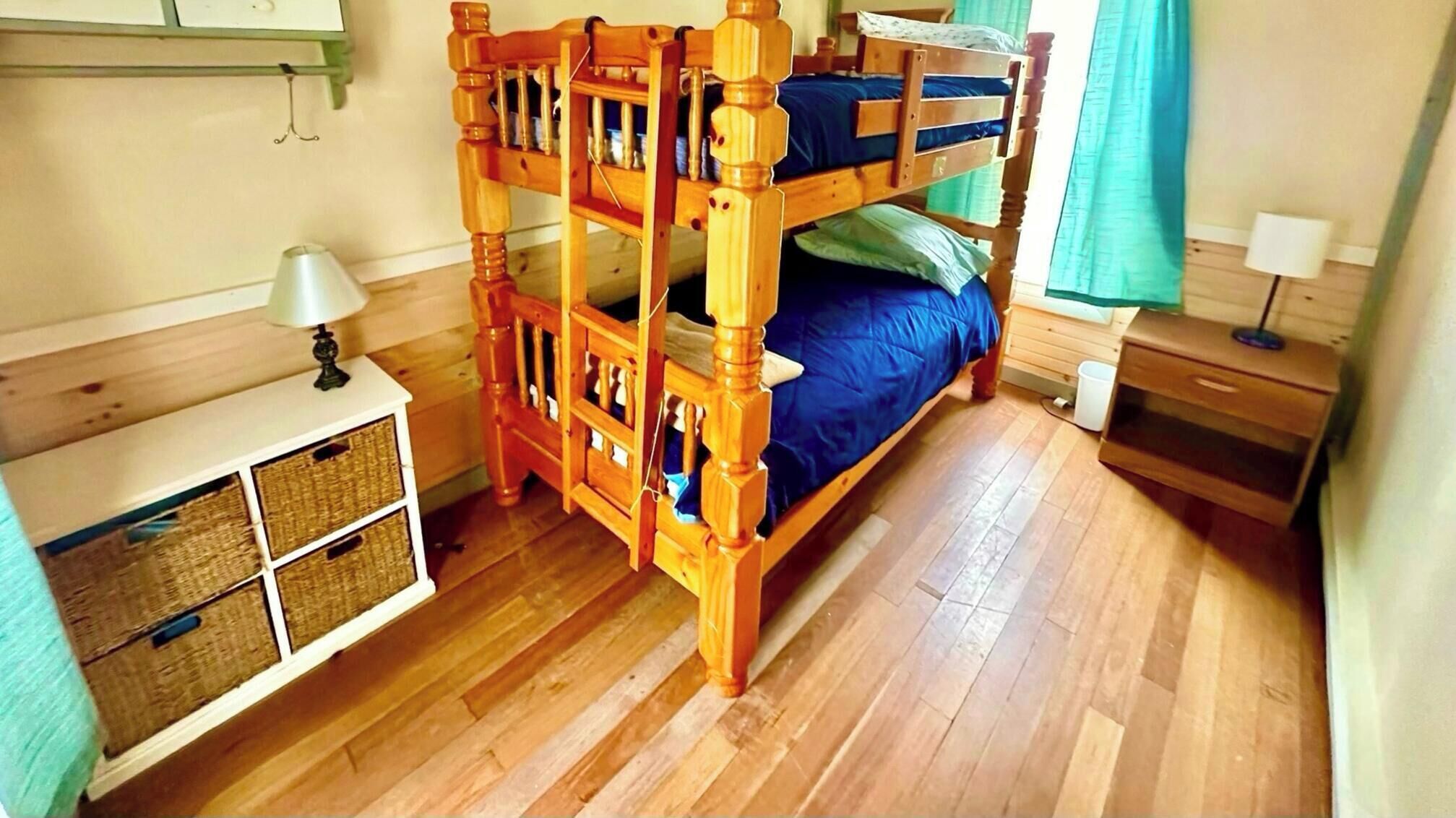 A bunk bed with a wooden frame, a bedside table with a lamp, and a small cabinet with baskets.