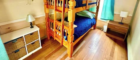 A bunk bed with a wooden frame, a bedside table with a lamp, and a small cabinet with baskets.