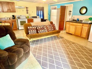 A living room with a sofa, a coffee table, and a kitchen area with appliances. - Peaceful 3-bedroom Cabin in Verona Beach (Verona Beach)