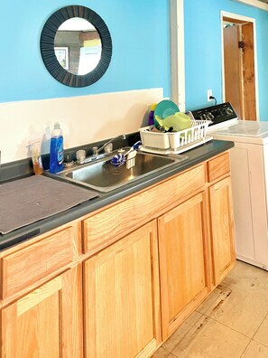 A kitchen with wooden cabinets, a black countertop, a sink, and a mirror above it. - Peaceful 3-bedroom Cabin in Verona Beach (Verona Beach)