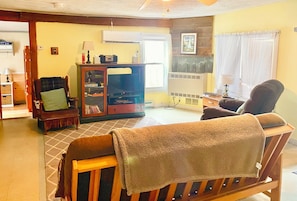A living room with a sofa, a television, a cabinet, and a window with curtains. - Peaceful 3-bedroom Cabin in Verona Beach (Verona Beach)