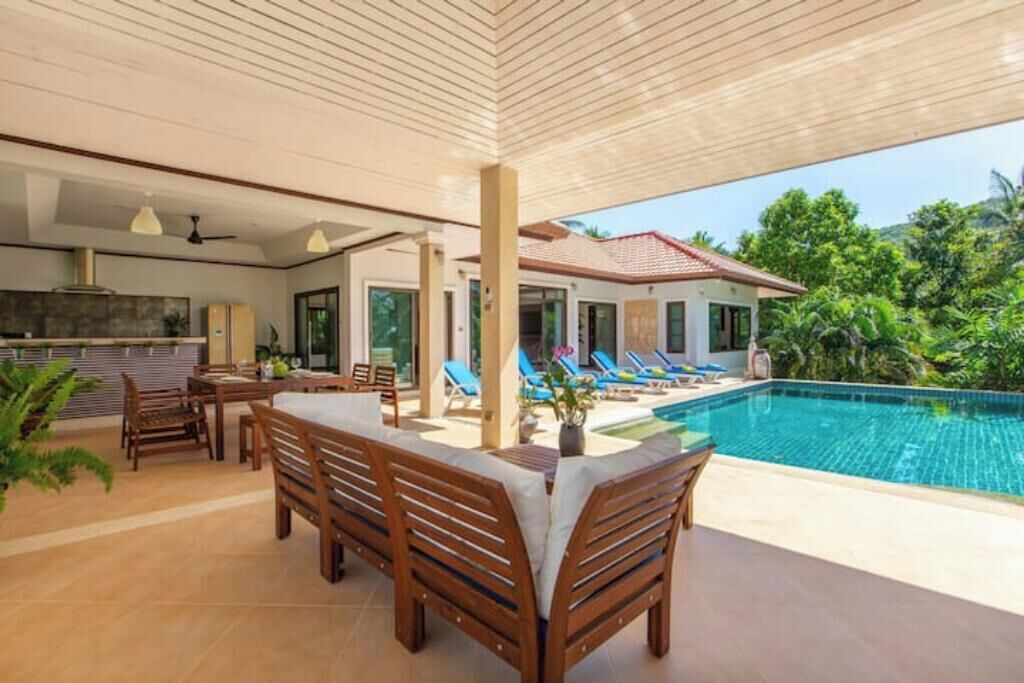 A modern outdoor living area with a pool, wooden furniture, and a view of a house.
