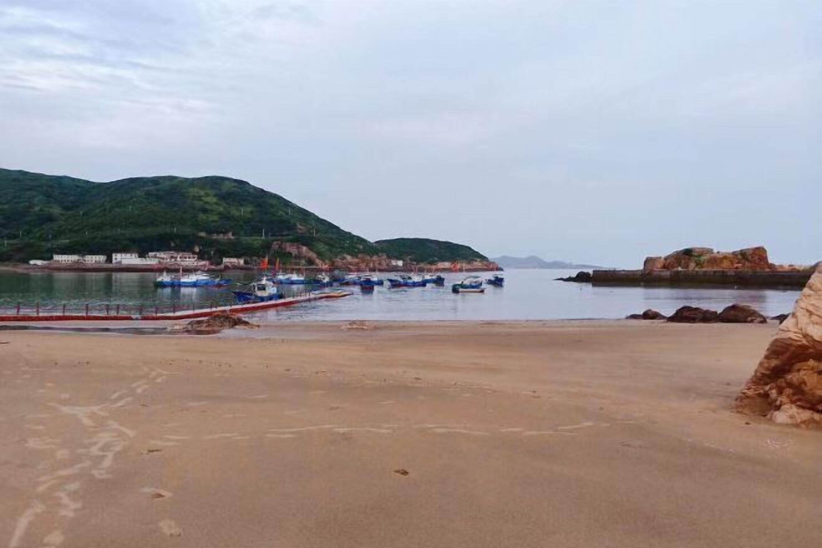 A beach with boats, a rocky outcrop, and a distant hill.