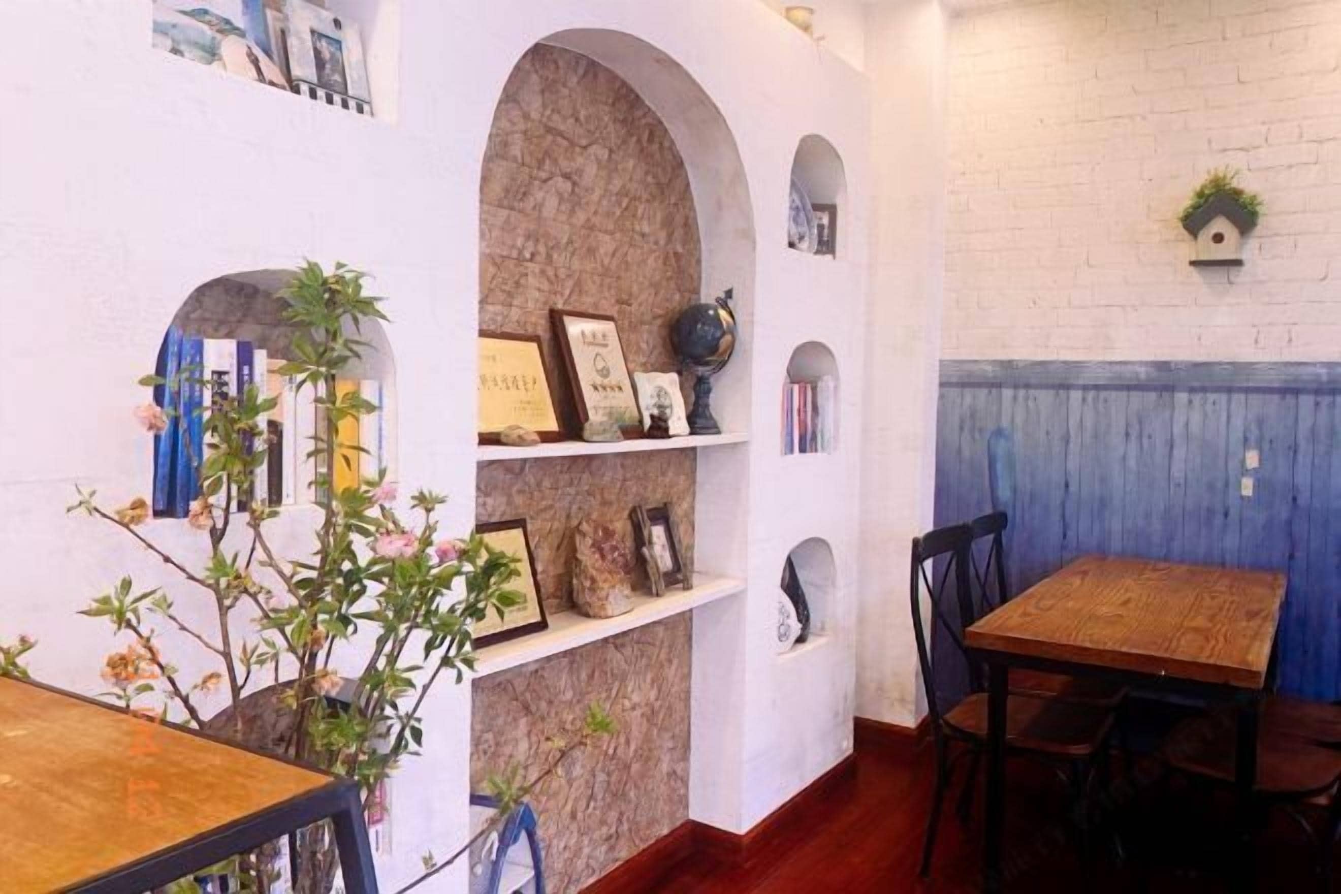 A dining area with a brick wall, shelves with framed items, and a wooden table.