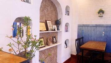 A dining area with a brick wall, shelves with framed items, and a wooden table.