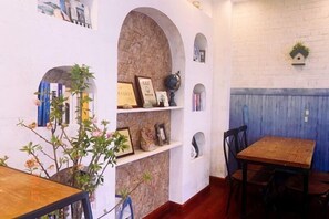 A dining area with a brick wall, shelves with framed items, and a wooden table.