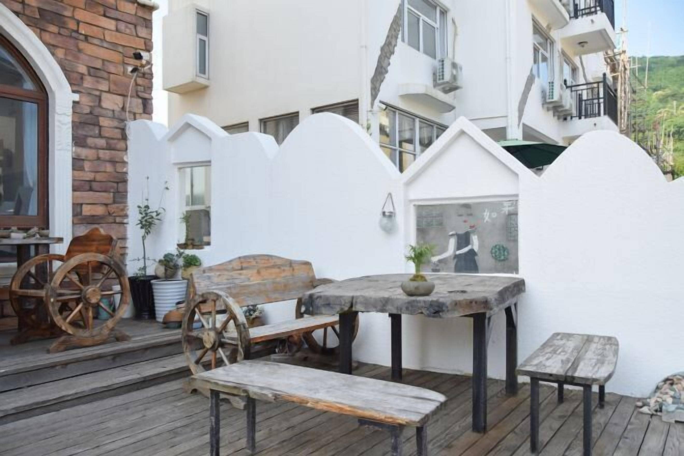 A wooden deck with a table and benches, a brick wall, and a white building with a window and a door.