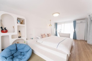 Une chambre d’hôtel comprenant un lit, un bureau, une chaise, une armoire et une étagère intégrée où sont rangés divers objets.