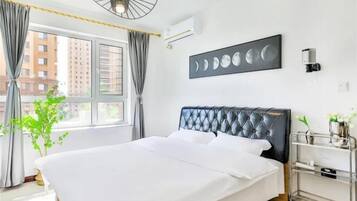 A hotel room with a bed, a bedside table, a wall-mounted air conditioner, and a window with curtains.