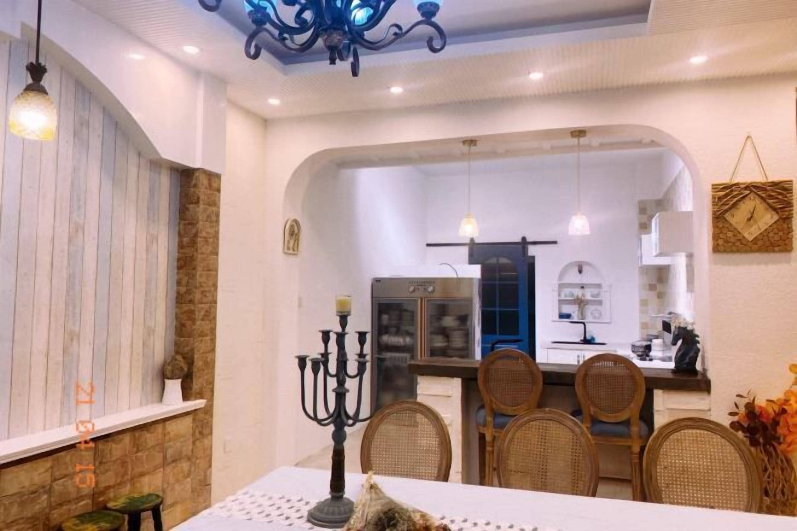 Comedor con una mesa dispuesta para cuatro, un candelabro como centro de mesa y una cocina visible a través de un arco.