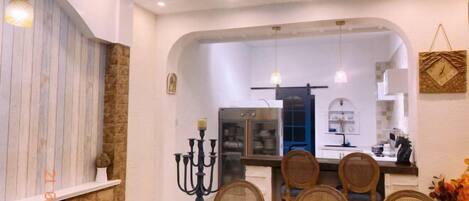 Comedor con una mesa dispuesta para cuatro, un candelabro como centro de mesa y una cocina visible a través de un arco.