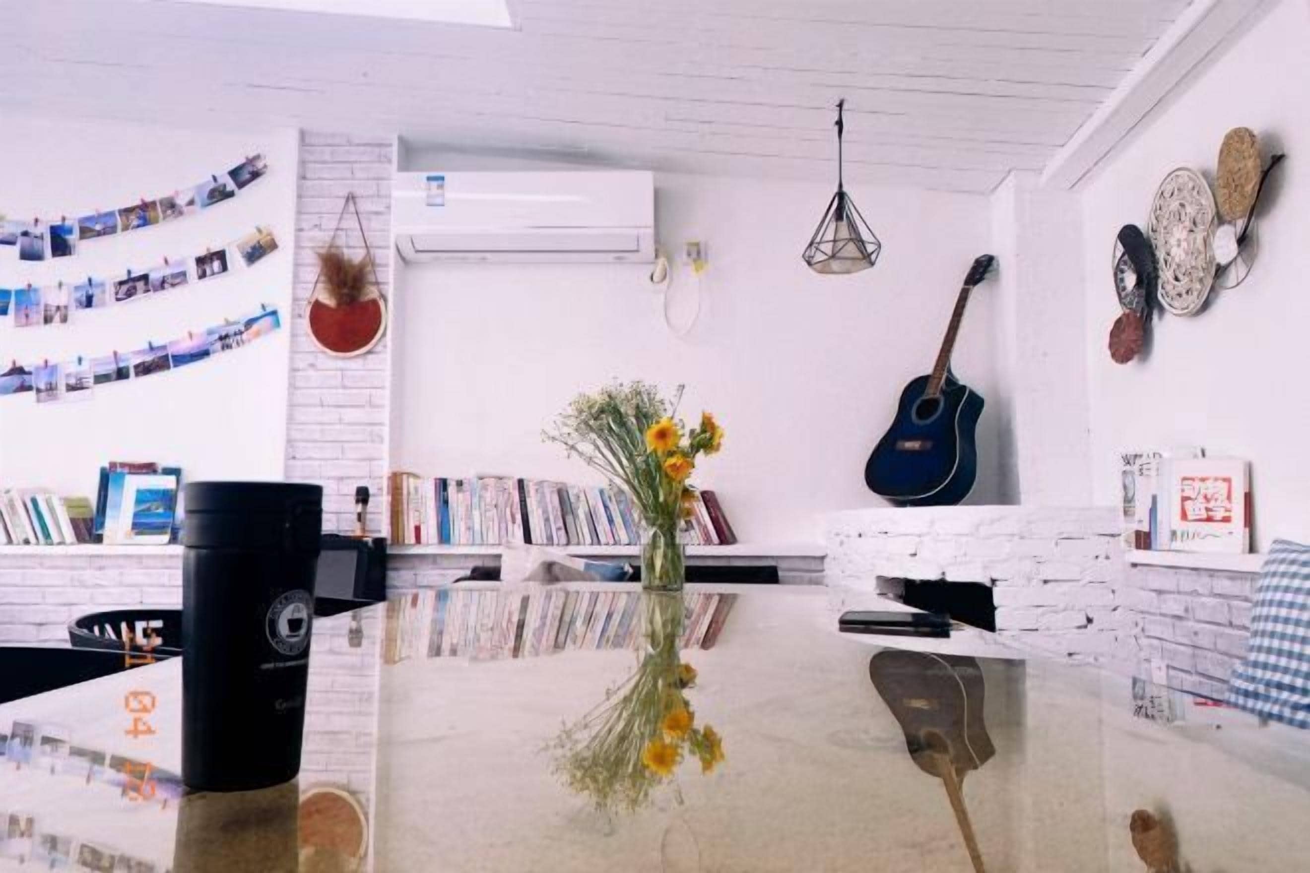A room with a glass table, bookshelves, a guitar, and a vase with flowers.