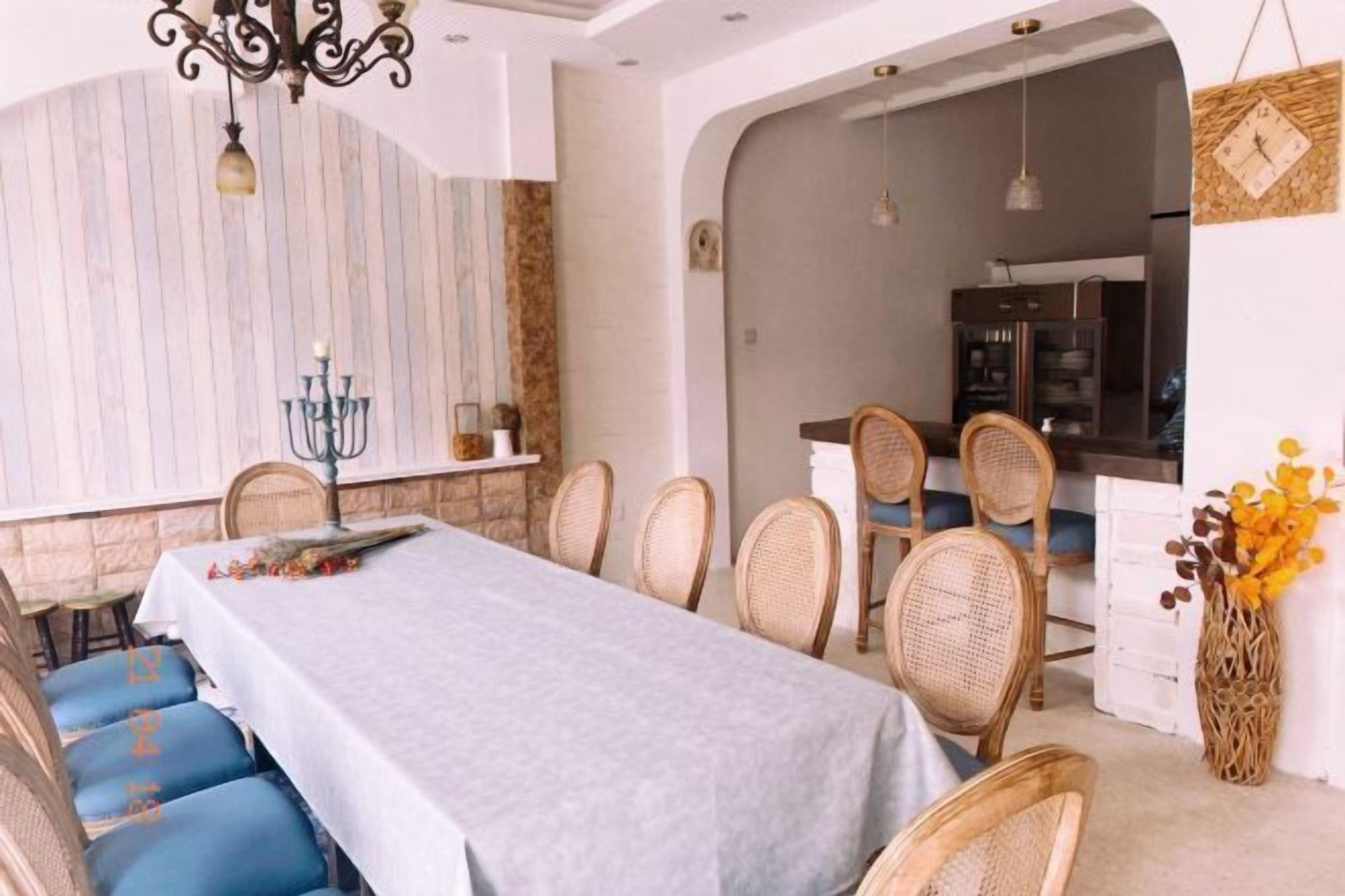 A dining area with a long table, blue cushioned chairs, wicker chairs, and a chandelier.