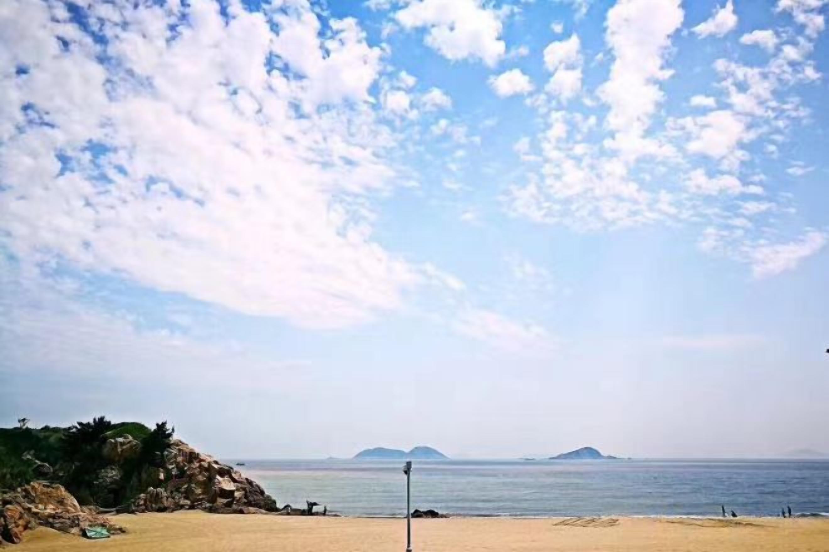 A beach with a clear sky, calm sea, and distant islands.