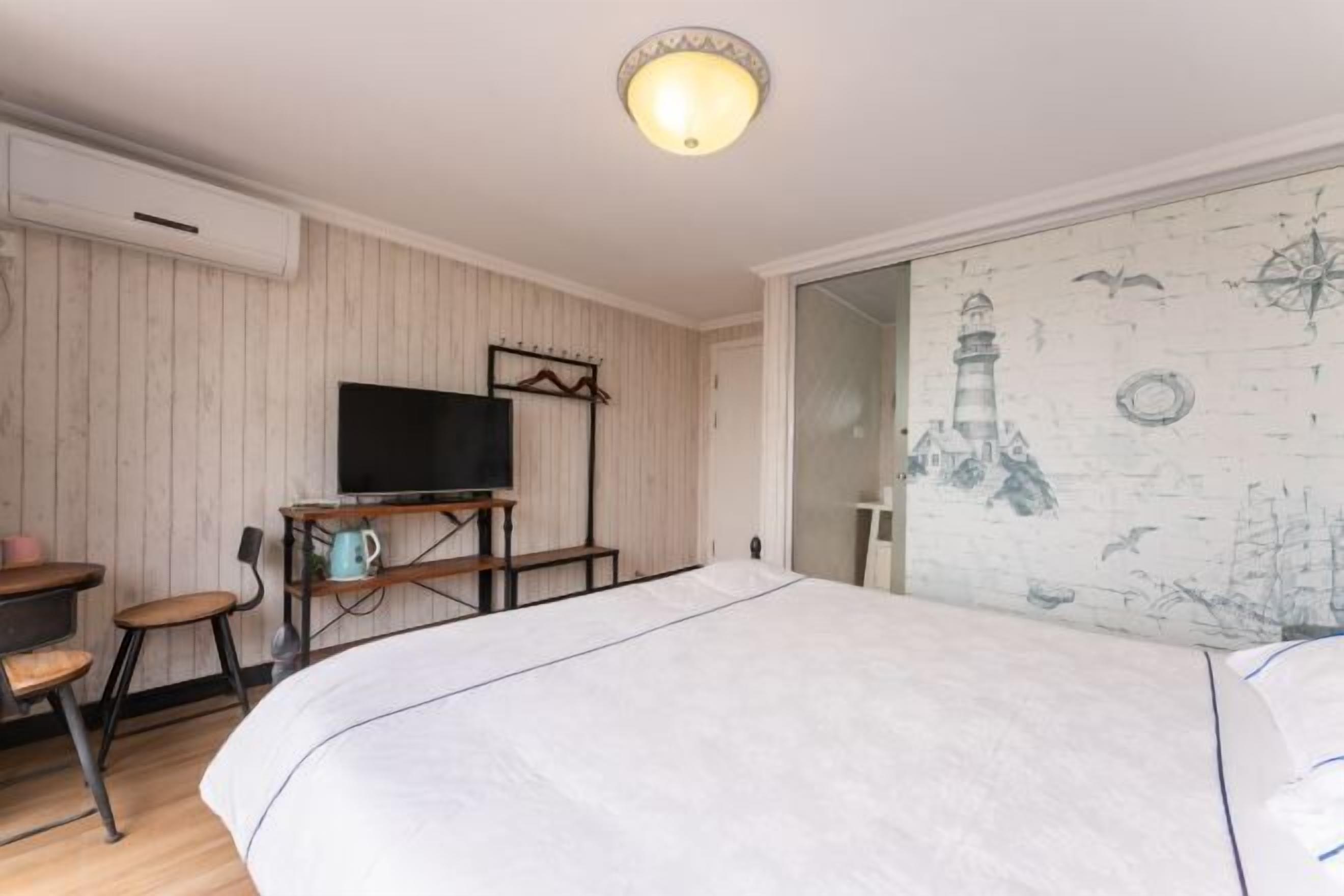 Un dormitorio con cama, televisor sobre un mueble, escritorio con silla y una pared decorada con motivos náuticos.