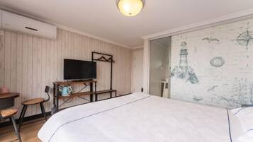 Un dormitorio con cama, televisor sobre un mueble, escritorio con silla y una pared decorada con motivos náuticos.