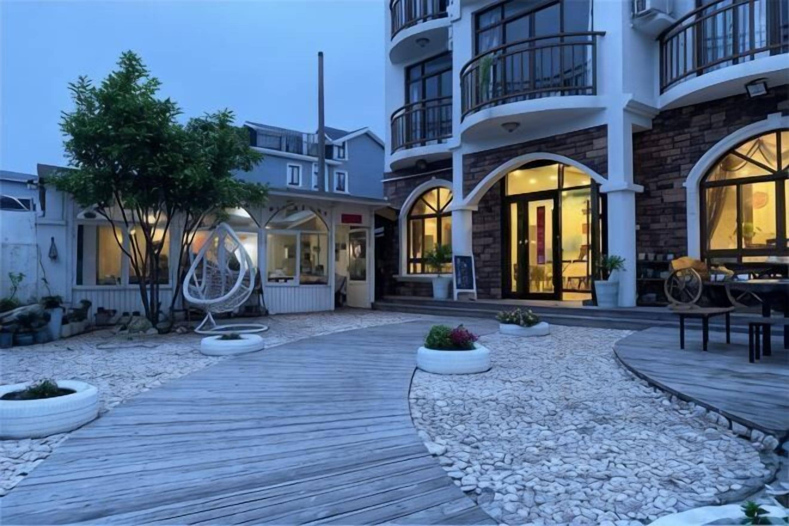 Un hotel con terraza de madera, mobiliario exterior y un edificio con varios balcones y grandes ventanales.