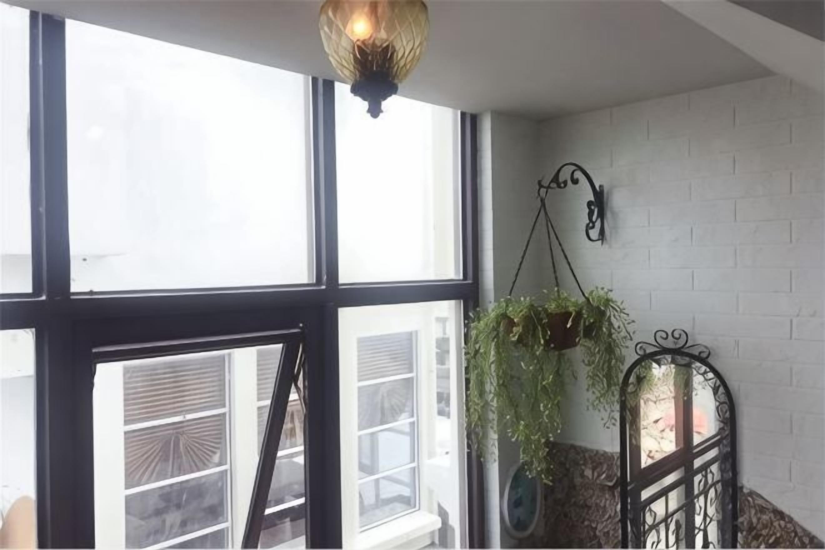 Et værelse med store vinduer, en hængende plante og en metalbænk.