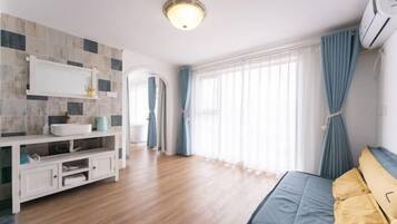 A modern room with a wooden floor, a bed with yellow pillows, a white sink, and a window with curtains.