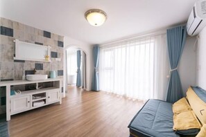 A modern room with a wooden floor, a bed with yellow pillows, a white sink, and a window with curtains.