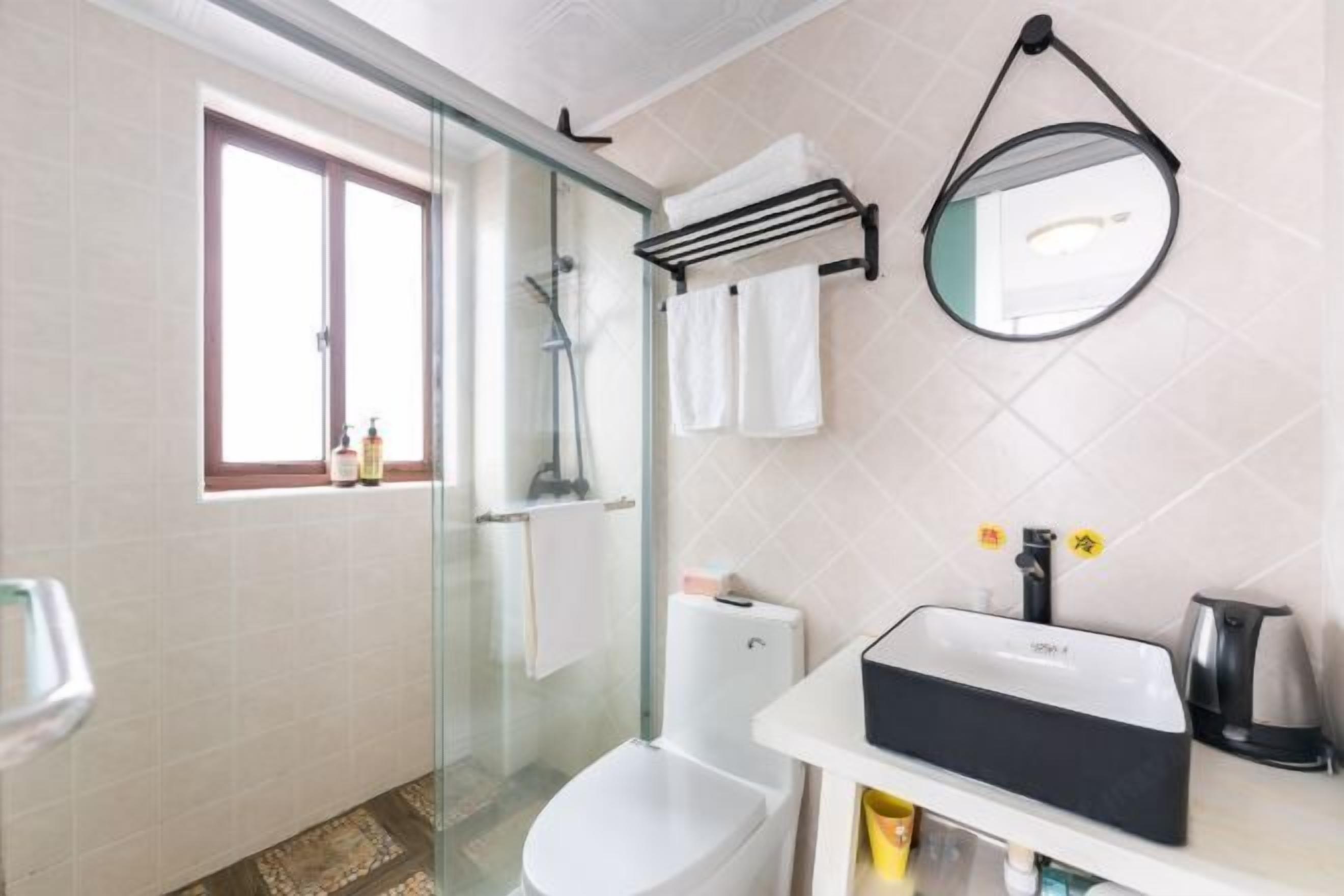 A bathroom with a glass-enclosed shower, a toilet, a sink with a black soap dispenser, and a mirror on the wall.
