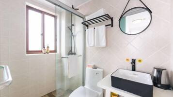 A bathroom with a glass-enclosed shower, a toilet, a sink with a black soap dispenser, and a mirror on the wall.