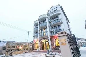 A multi-story hotel with a prominent entrance, balconies, and a gated driveway. - Shengsi painted shatinghai Homestay (Shengsi)