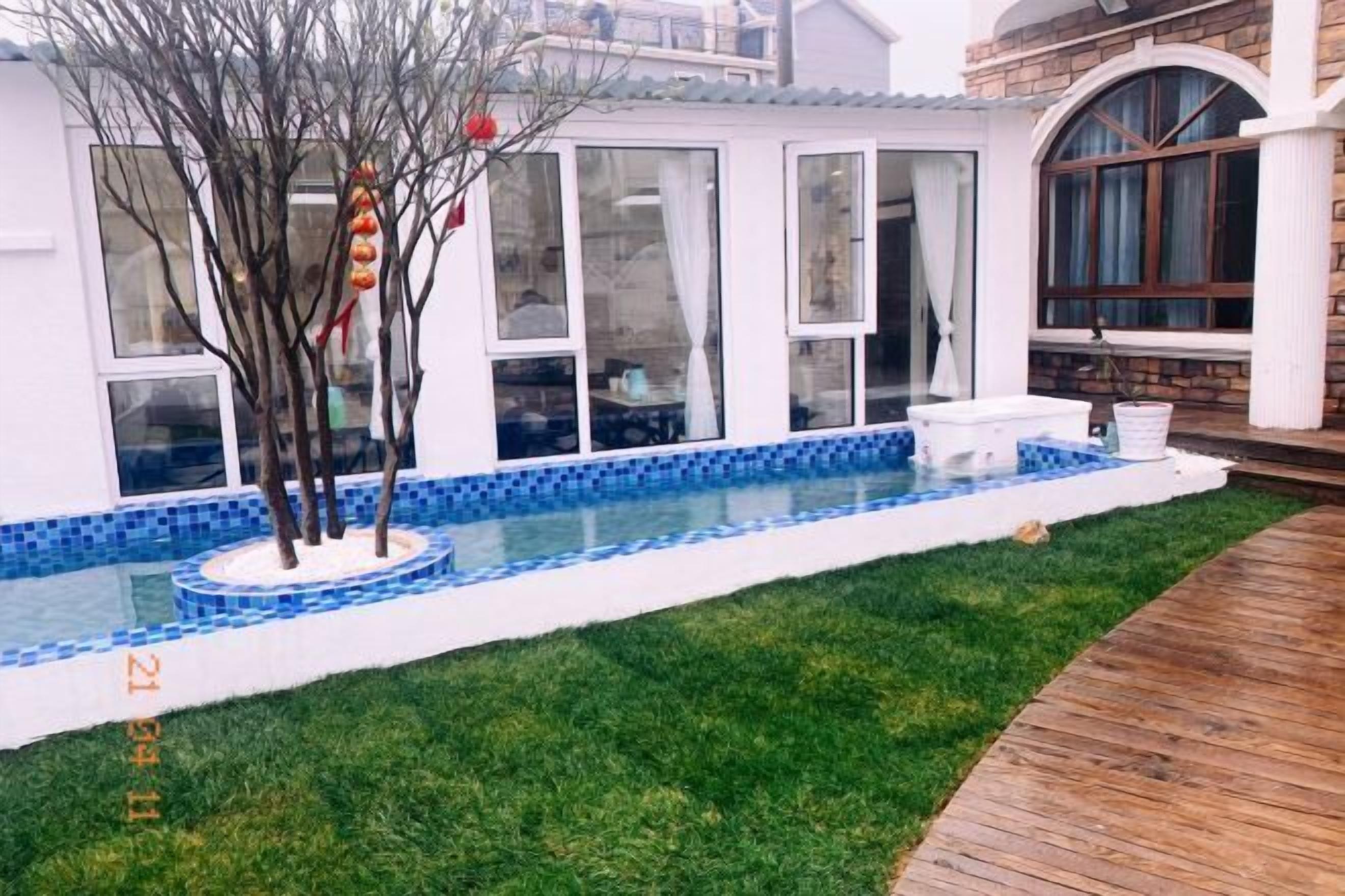 A swimming pool with a tiled edge, a grassy area, and a wooden deck.